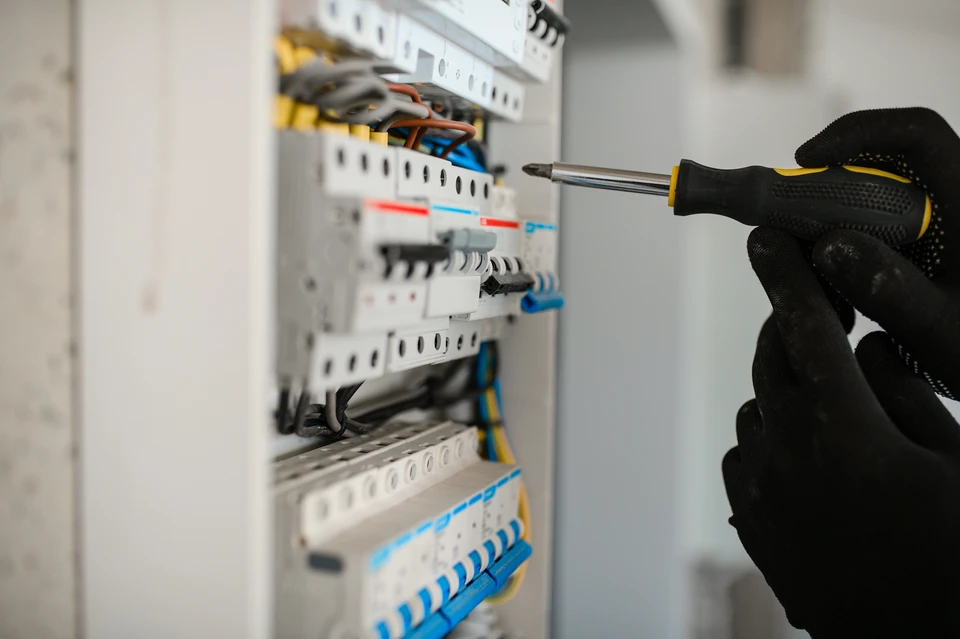 Électricien professionnel travaillant dans un tableau électrique domestique, manipulant des câbles multicolores avec des outils spécialisés